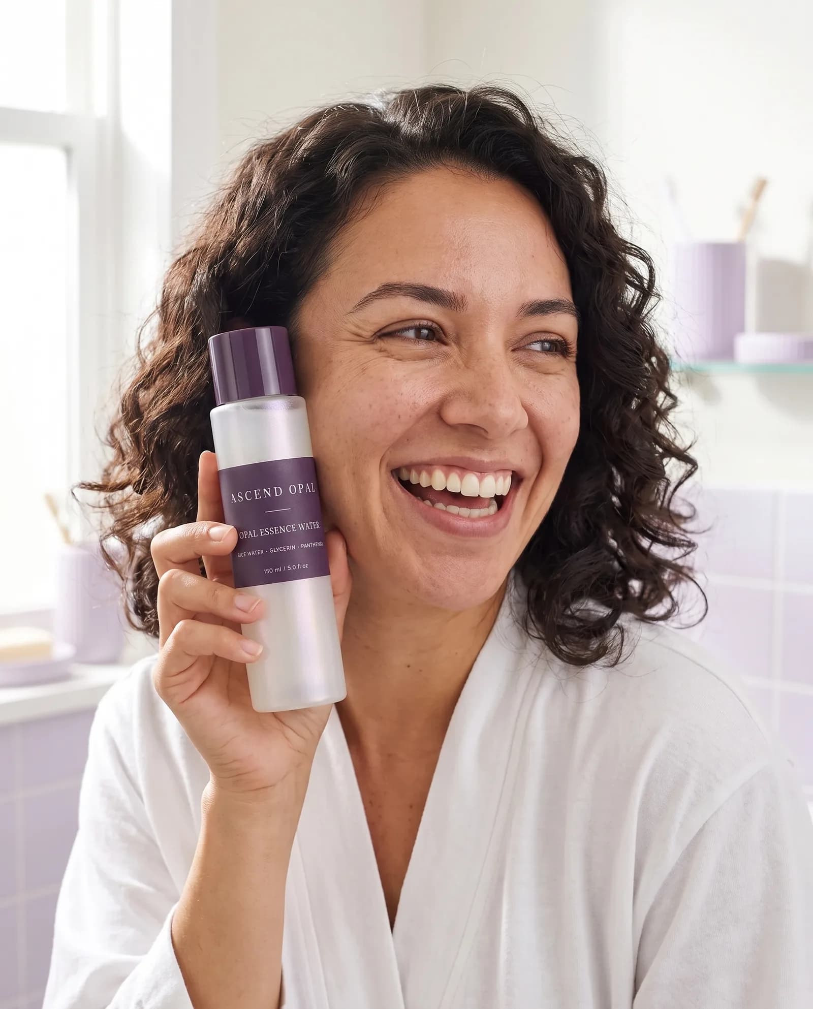 A woman in a white robe laughing, holding a bottle of Opal Essence Water beside her cheek